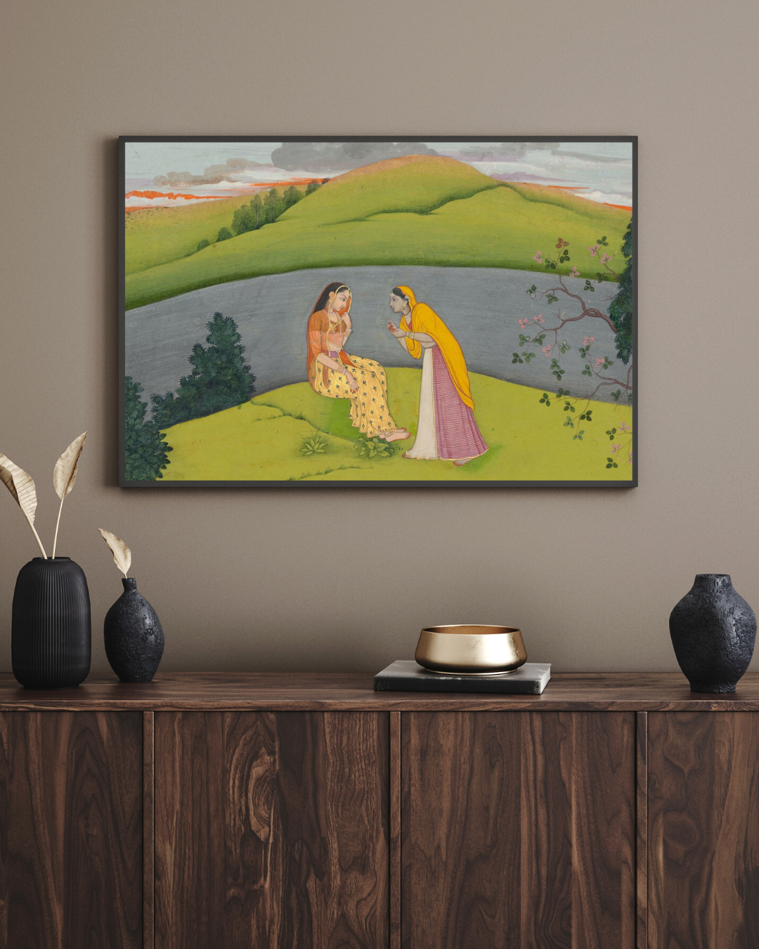 Framed artwork of two women sitting by a lake on a wall above a wooden console table with decorative items.